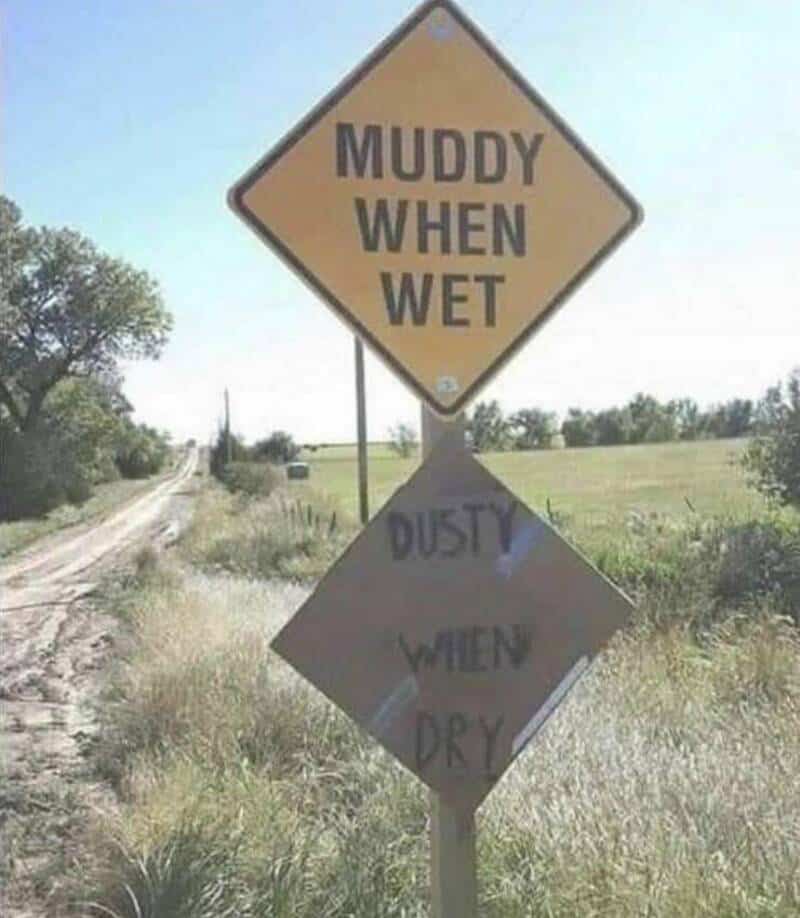 Sign says 'Muddy when wet' and 'Dusty when dry' in a rural area.