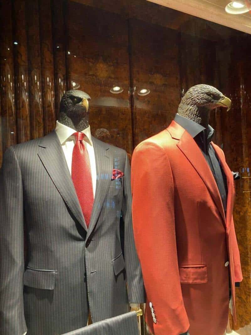 Two mannequins with bird heads dressed in suits, one in a gray pinstripe and the other in a red suit.