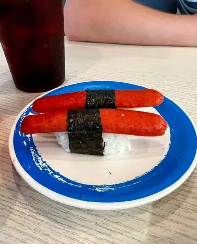 Sushi with two red sausages and seaweed on rice, on a blue plate.