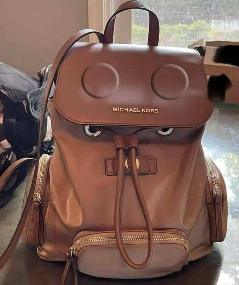 Michael Kors backpack with a face-like design on the flap, resembling eyes and a mouth.