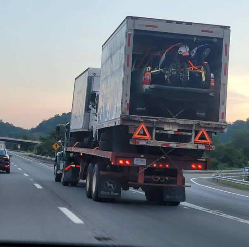 Truck carrying a motorcycle in a transparent container on the highway.