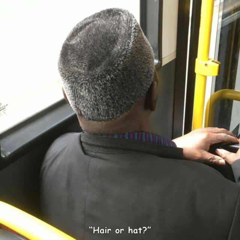 Man with a unique hairstyle or hat, sitting on a bus, looking out the window.