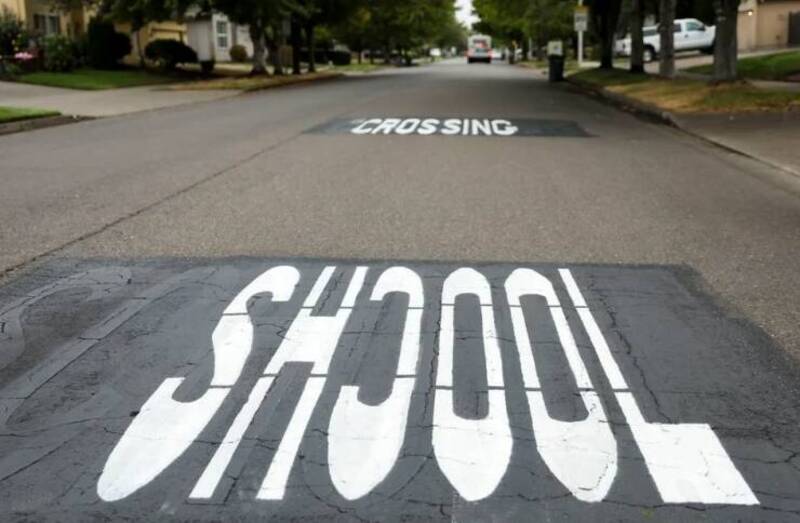 A street with a crosswalk painted with the word 'SCHOOL' and a 'CROSSING' sign.