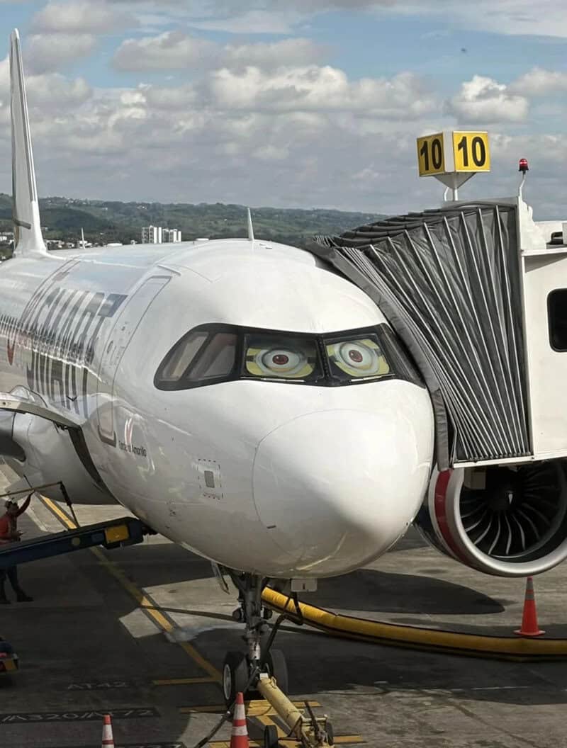 Airplane with cartoon eyes on the cockpit windows and a jet bridge attached.