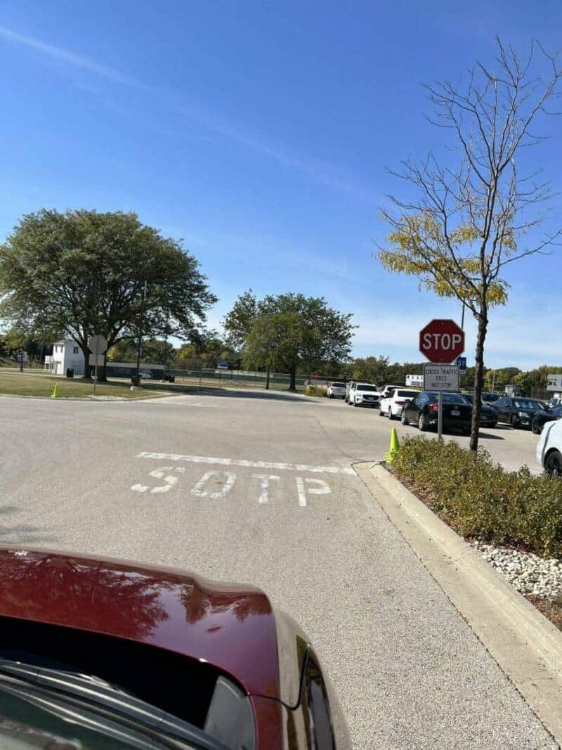 Stop sign and painted 'STOP' on the parking lot with trees and cars in the background.