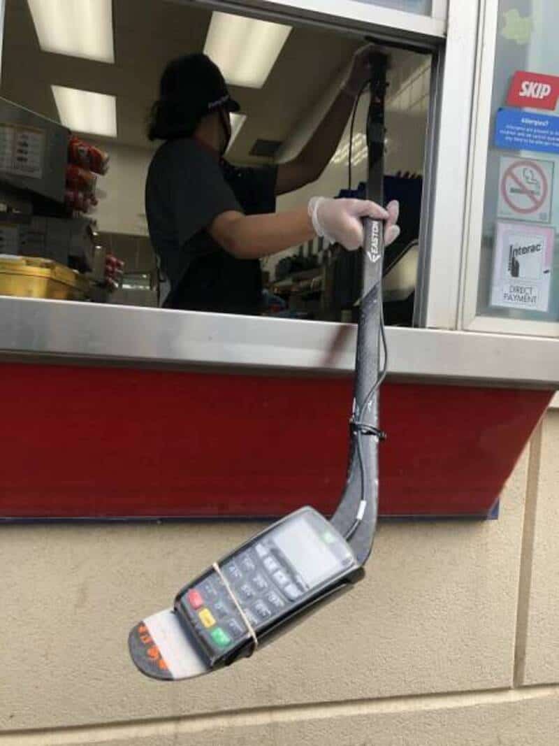A person at a drive-thru window holding a long pole with a phone attached, resembling a fishing rod.
