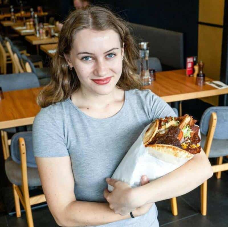 Young woman holding a large sandwich in a restaurant setting.