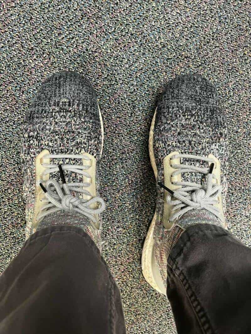 Pair of sneakers on a speckled floor, with black pants visible.