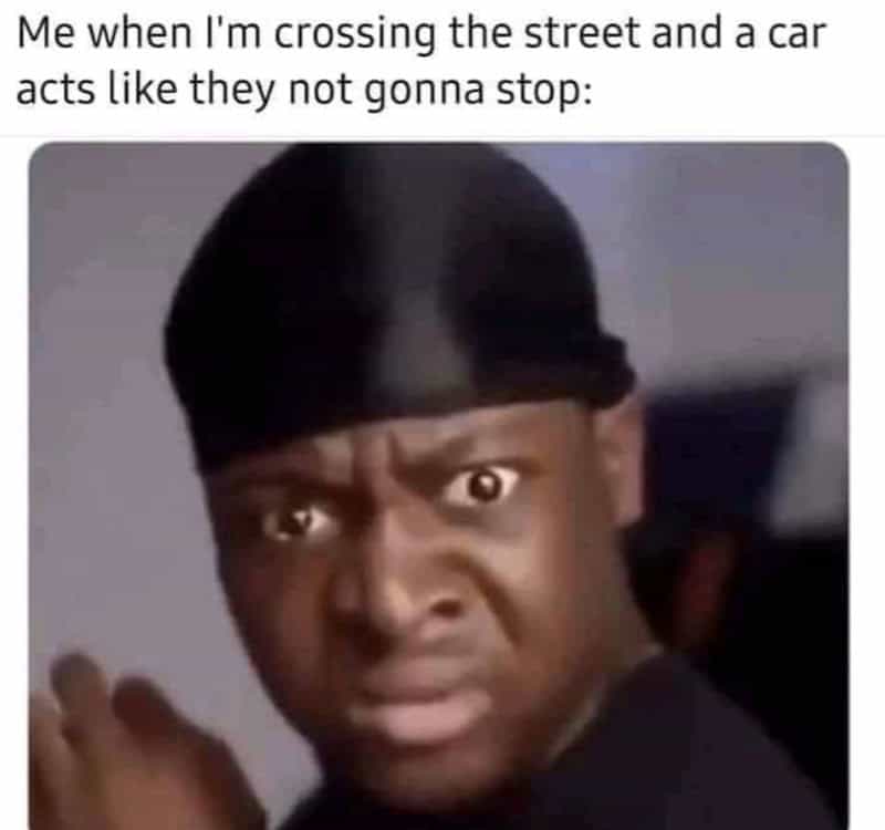 Person crossing street with a surprised expression, wearing a durag.