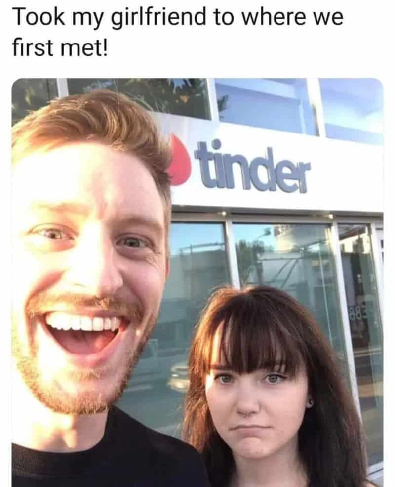 Couple taking a selfie outside Tinder office, woman looks unimpressed.
