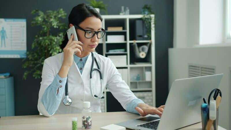 Female doctor on phone using laptop in clinic.