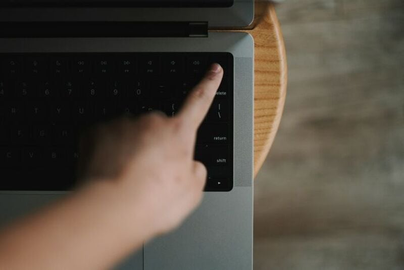 Person's finger pressing the delete key on a laptop keyboard.