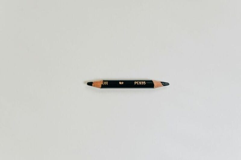 A black pencil with gold markings lying on a white surface.