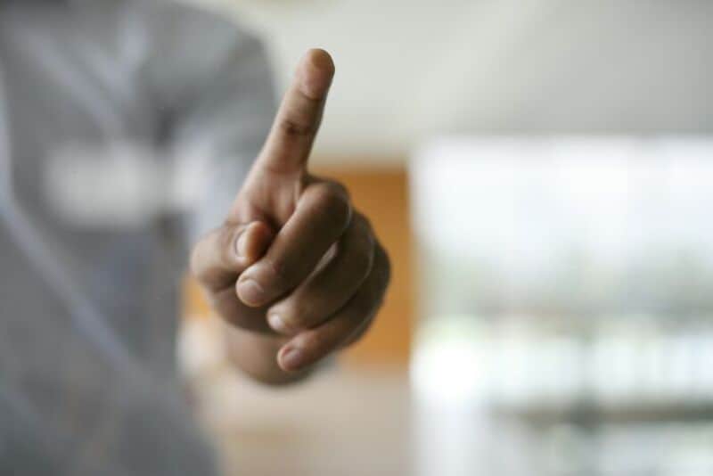 Person pointing with index finger in a blurred indoor background.