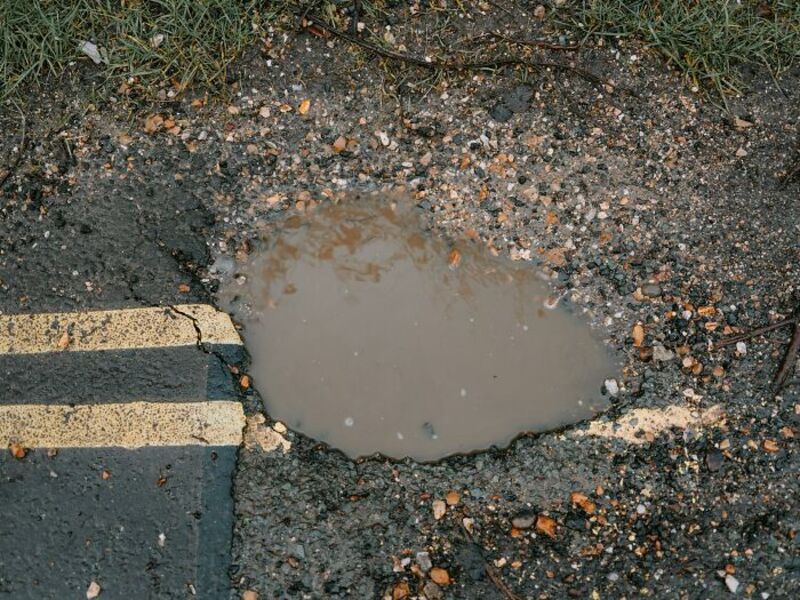 Pothole filled with muddy water on a road with yellow lines.
