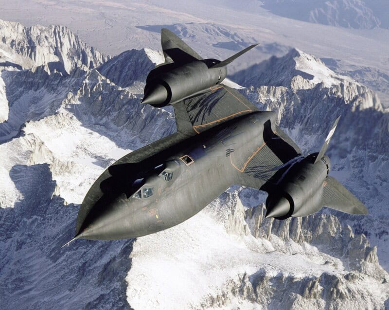 F-22 Raptor fighter jet flying over snowy mountains.