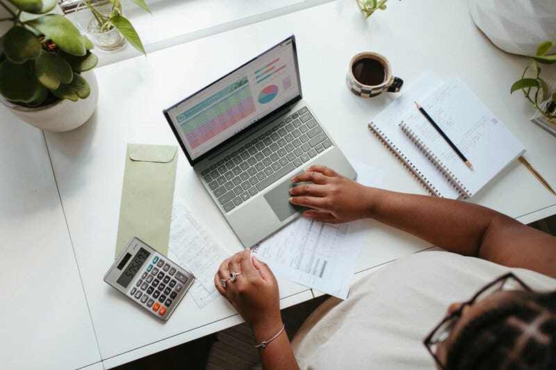 Person working at a desk with a laptop, calculator, notebook, and coffee.