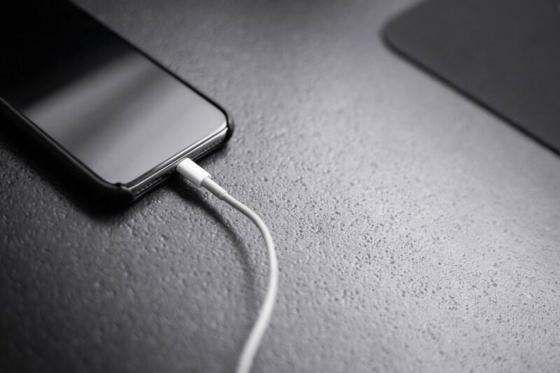 Smartphone connected to a charging cable on a textured surface.