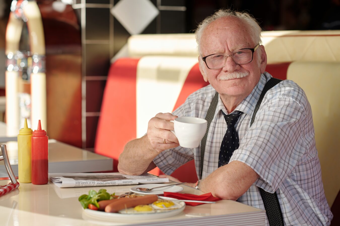 A cheerful elderly man enjoying breakfast at a diner.