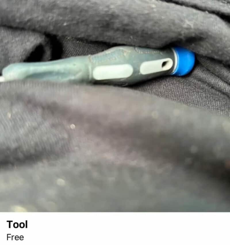 Small screwdriver with blue handle on dark fabric.