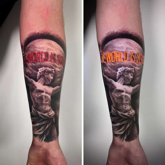 Tattoo of a classical statue with UV-reactive text 'The world is you' in red and orange.