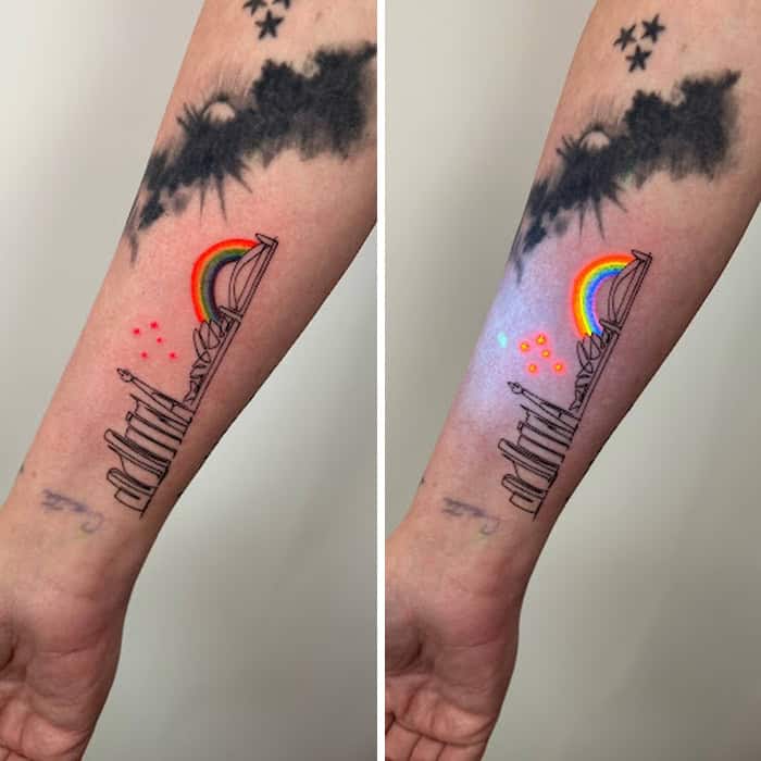 Tattoo of a rainbow, cityscape, and clouds on forearm, visible under UV light.