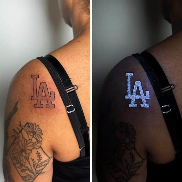 Tattoo of LA logo that glows under UV light on shoulder with floral tattoo below.
