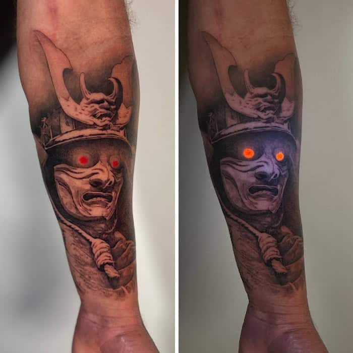 Tattoo of a demon with glowing red eyes under UV light.