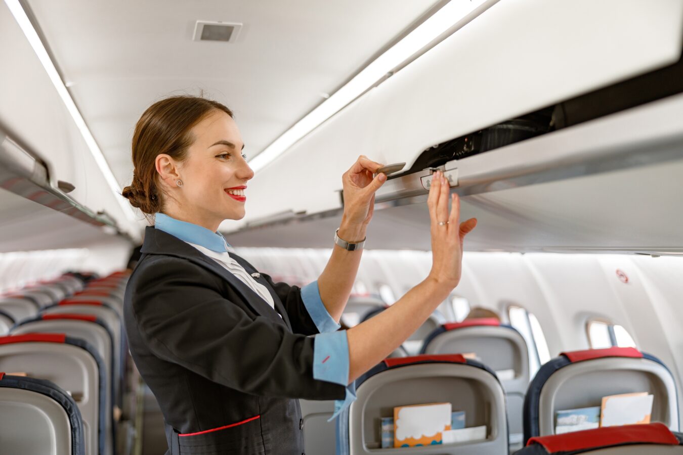 Flight attendant smiling and organizing overhead compartment on airplane.