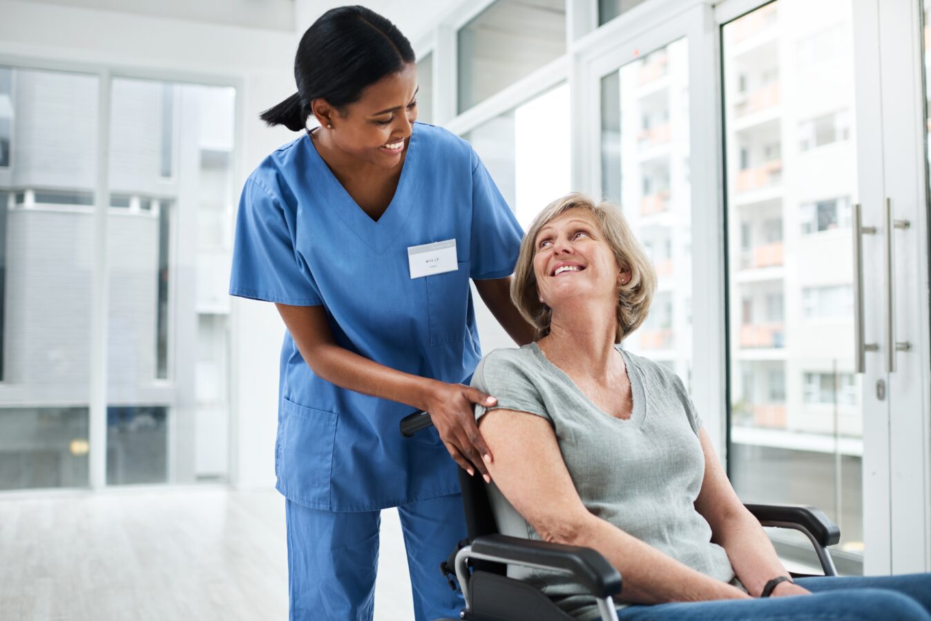 Nurse smiling at elderly woman in wheelchair in bright room.