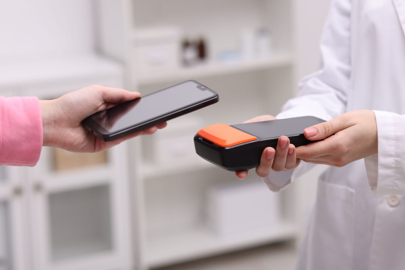 Person in pink sleeve hands over a smartphone to a person in a white coat holding a payment terminal.