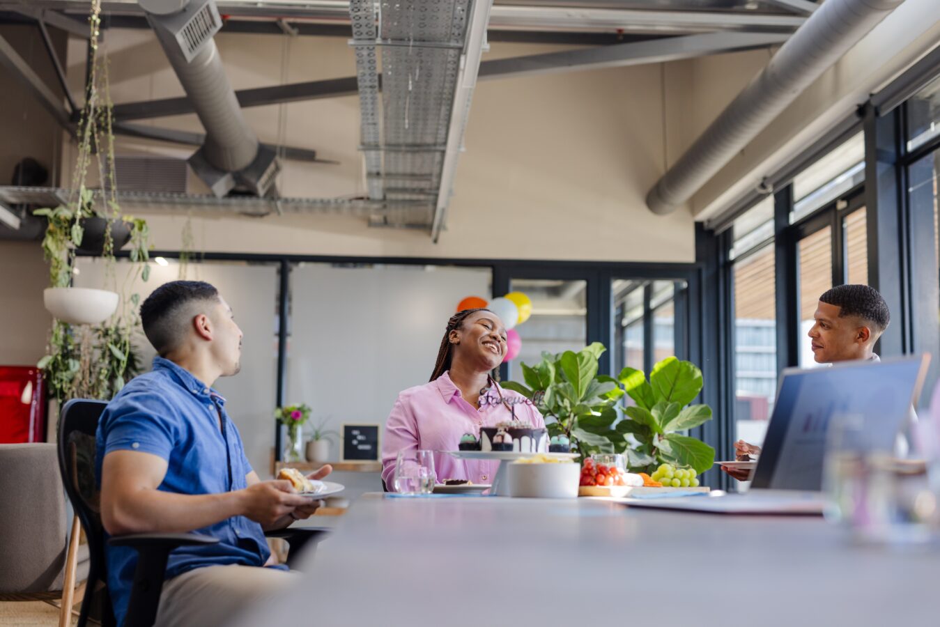 People sharing a meal and laughing together in a modern office space.