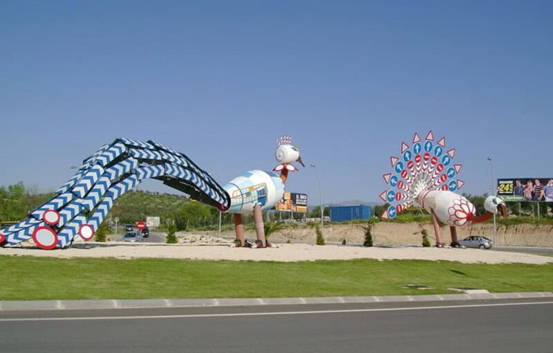 Large colorful sculptures of a snake, a snail, and a Ferris wheel on a roadside.