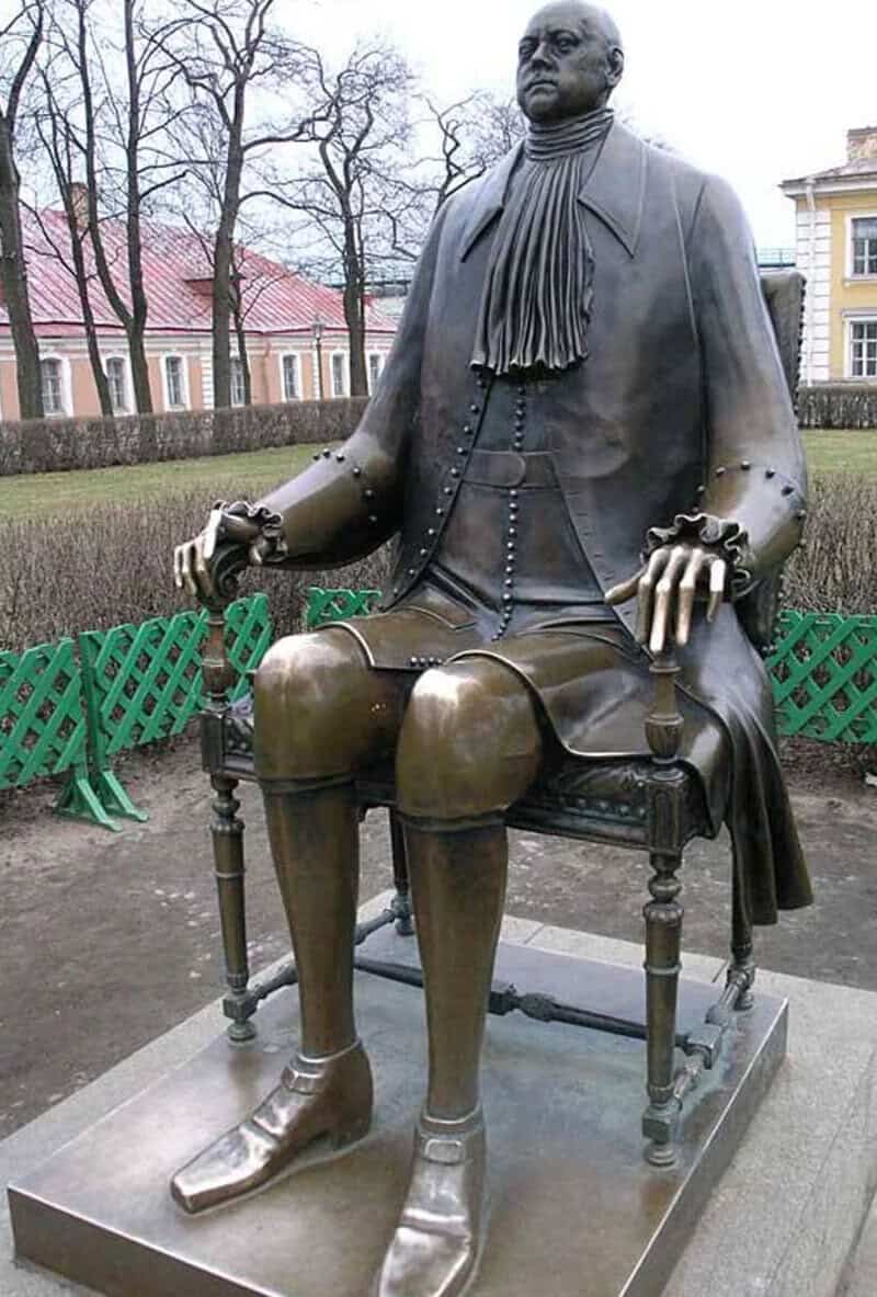 Bronze statue of a seated man in historical attire on a park bench.