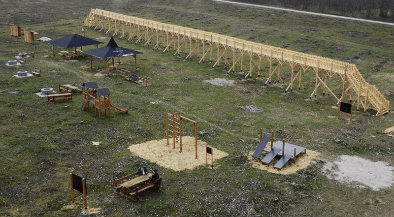 Elevated wooden obstacle course on grassy field with playground equipment.