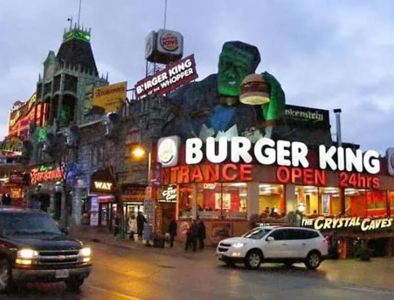BURGER KING sign with large Hulk figure and other neon signs on a busy street at night.