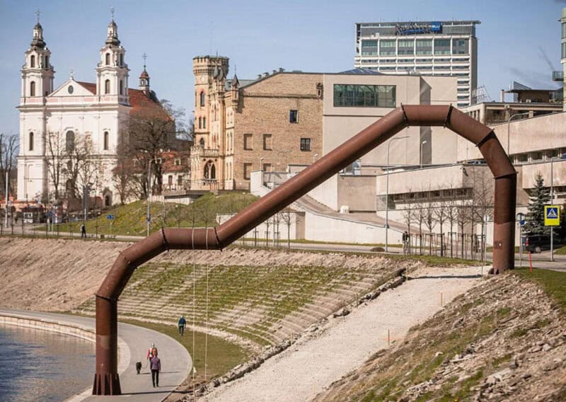 Large brown industrial pipe structure crossing a river in an urban area.