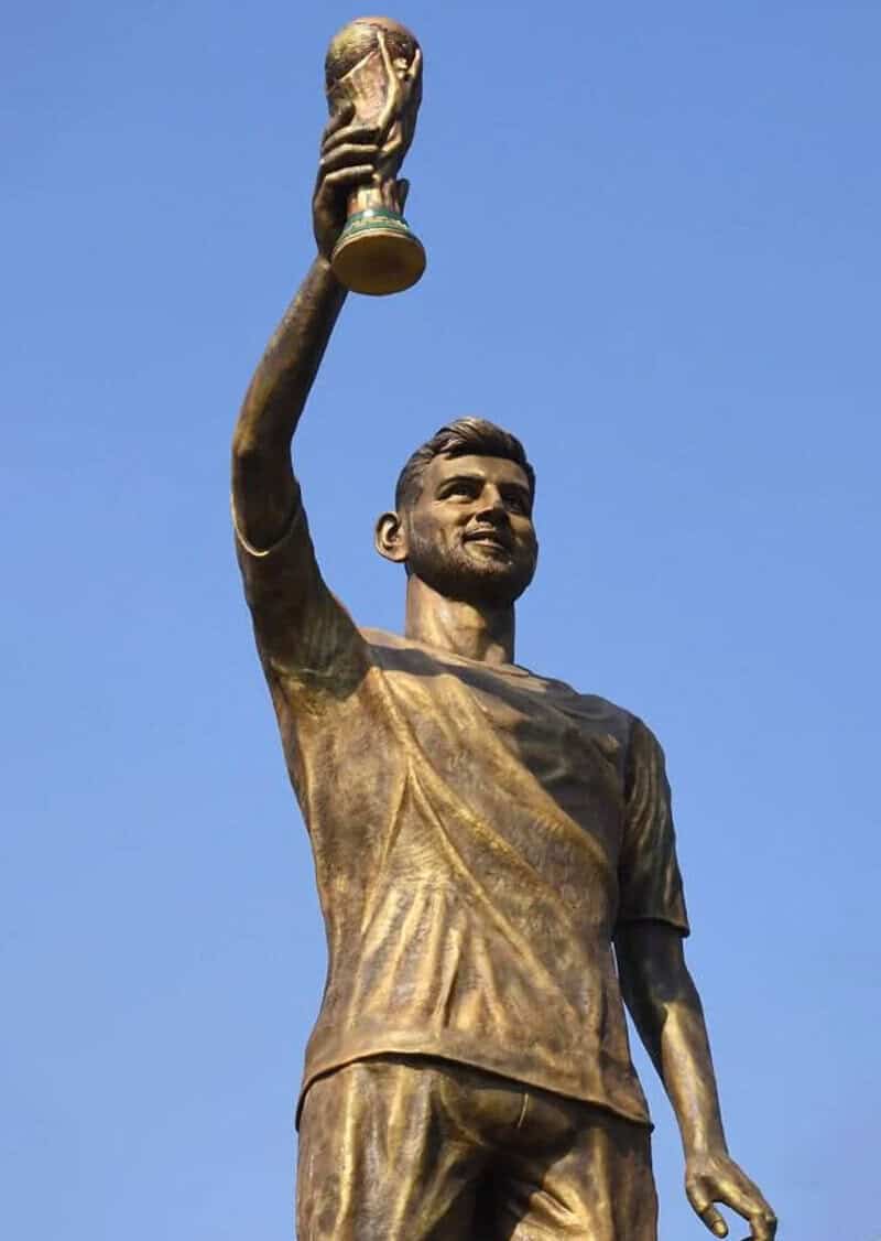 Statue of a man holding a trophy up high against a blue sky.