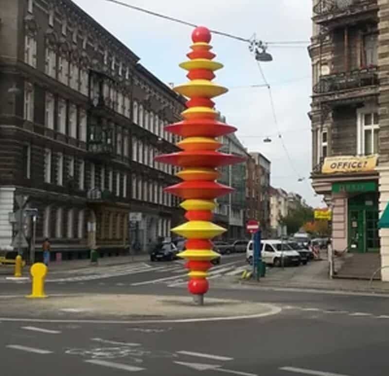 Colorful stacked disc sculpture on city street corner, urban background.