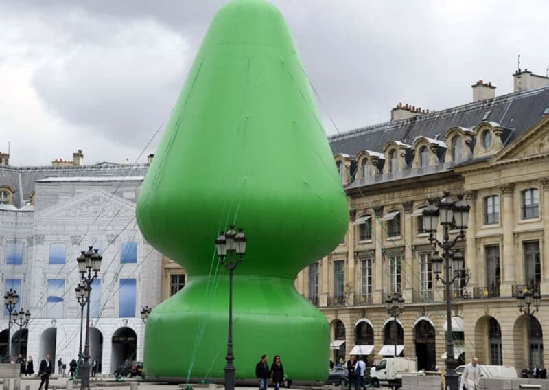 A giant green sculpture resembling a Christmas tree in a city square.