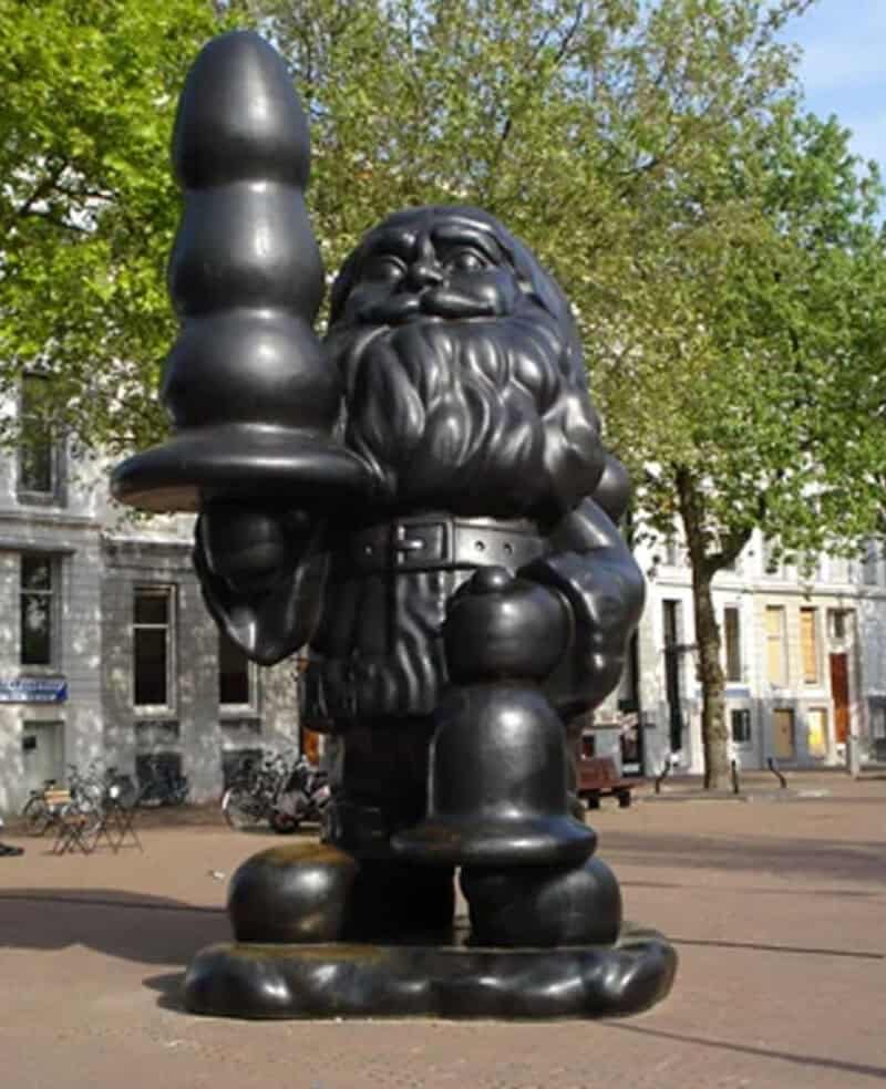 Large black gnome statue holding a candle in an outdoor park setting.