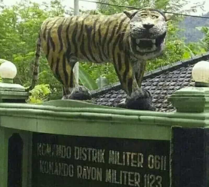 Tiger statue on a green roof with trees in background.