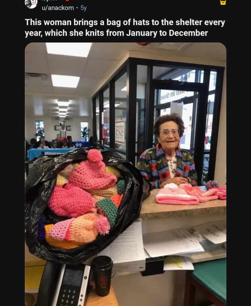Elderly woman with glasses and colorful sweater at shelter counter with knitted hats.