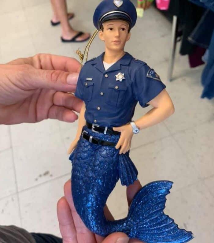Blue police officer doll with mermaid tail, held by a hand, in a store setting.