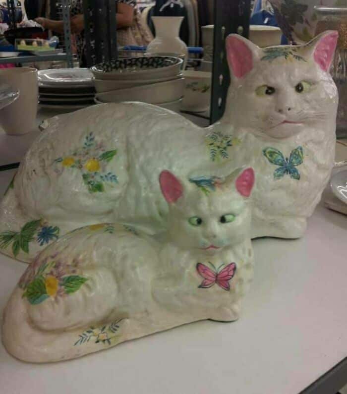 Ceramic cat sculptures with painted flowers and butterflies on a table.