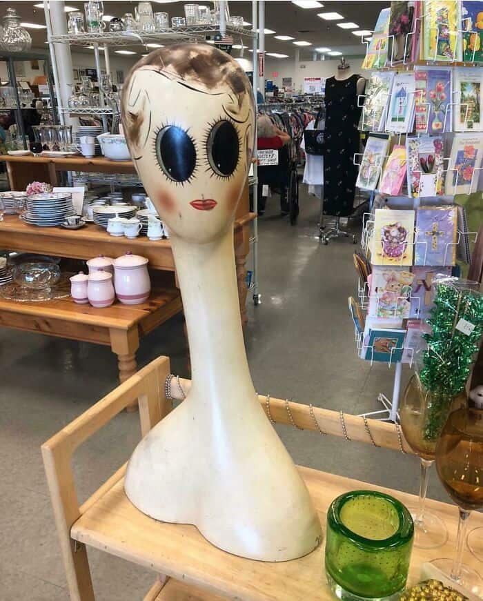 Vintage doll head lamp with large eyes and painted face on a wooden table in a store.