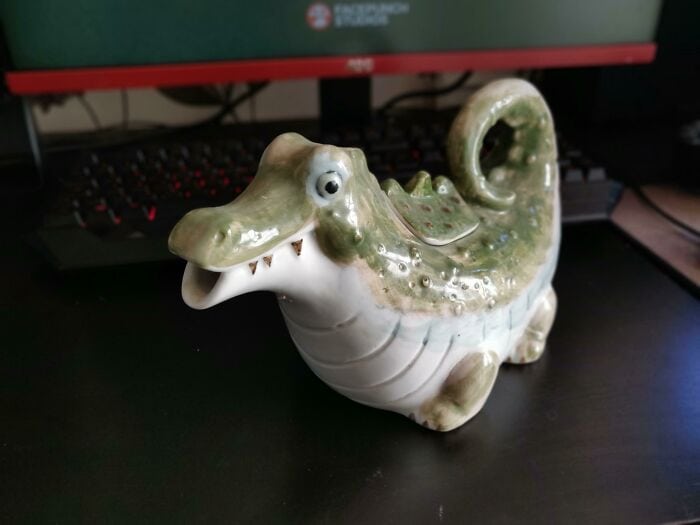 Ceramic crocodile figurine with a smiling face on a desk.