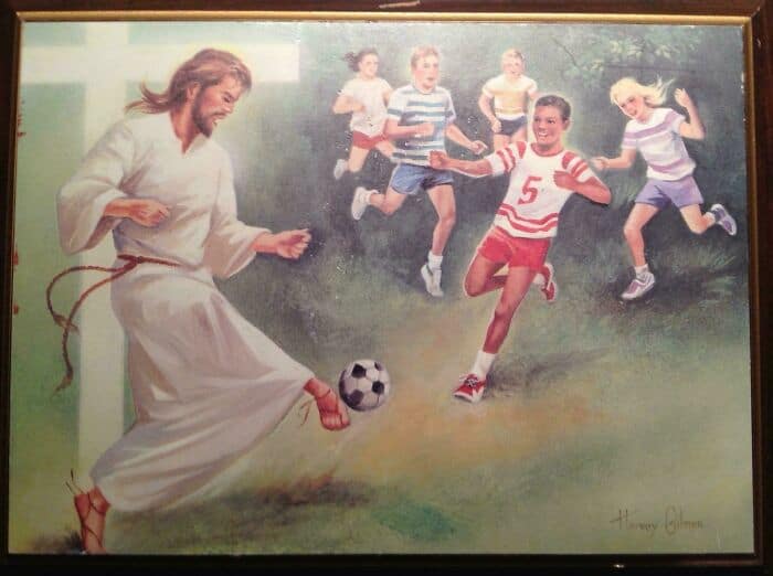 A woman in a white karate gi kicking a soccer ball while children run and play behind her.