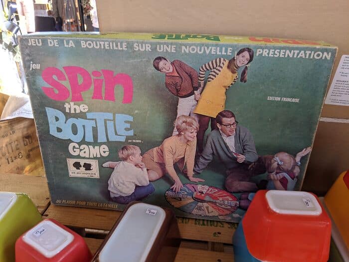 Spin the Bottle game box with five children and two adults playing on a green table.