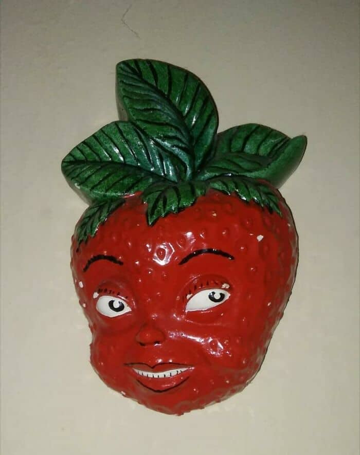 Strawberry character with a smiling face and green leaves on top.